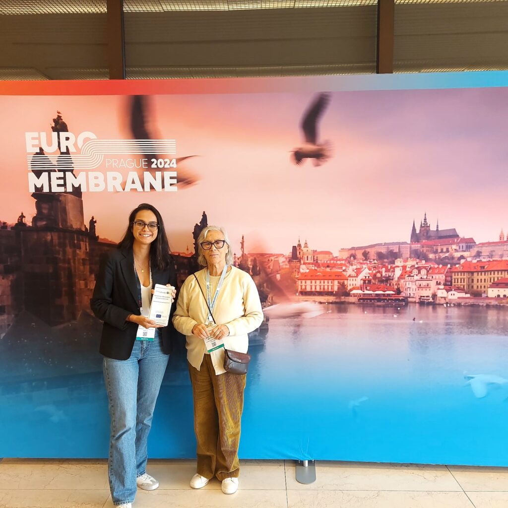 Maria Norberta de Pinho and Camila Cabeza standing in front of a huge Euromembrane 2024 Poster