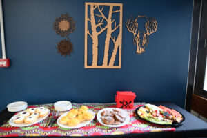 A table with four plates with some snacks. Above is some wooden africen art on the dark blue wall