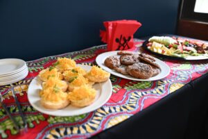 trhee white plates with snacks, cookies, cheese and vegetables on a colorful tablecloth in front of a dark blue wall